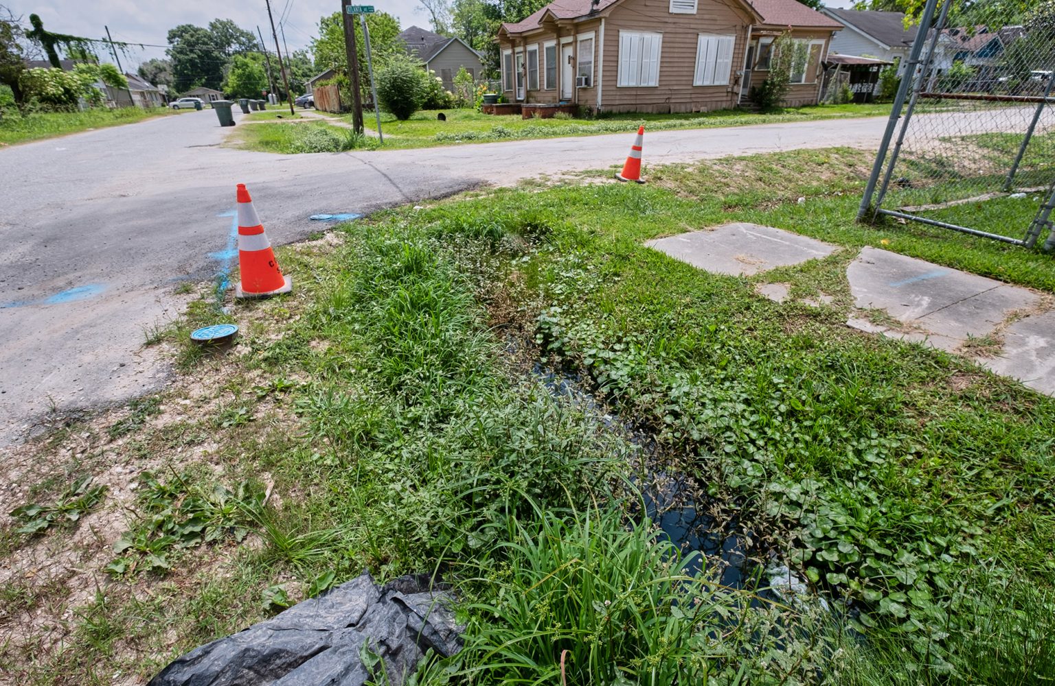 Safety cones mark an area of standing water and overgrown vegetation on Atlanta Avenue in a Beaumont, Texas neighborhood May 17, 2022. Throughout the year, and especially during hurricane season, Beaumont residents face environmental hardships like flooding, sewage overflow, foul smells, air pollution from nearby oil refineries and a lack of recovery funding.